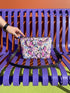 Small vegan leather crossbody purse with a real pebble grain texture and adjustable black strap. The flat printed artwork features a scattered all over pattern of pink skulls, purple and pastel blue winged bats, pink fanged mouths, and loose eyeballs set against a cream colored background. The bag is shown with black and silver hardware including a black top zipper, black zipper pull, black strap tabs, and silver metal rings and clips. The compact rectangular bag measures 8.5 by 7 by 2 inches.