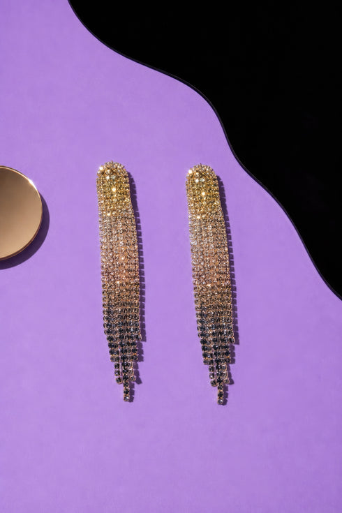 a pair of gold dangling earrings with a cascading tassel design, placed on a purple background.
