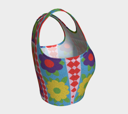 A high-resolution product photo of a body-hugging, 2D printed crop top with a 1970s-inspired floral patchwork pattern. The design consists of vibrant squares in cobalt blue, pale lavender, and deep violet, separated by pink borders with red dots. Central motifs include yellow daisies with orange centers and green-magenta floral mandalas. The top is made of a smooth, high-stretch performance knit fabric with curved back armholes and a cropped waistline.