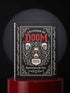 An 8.5 x 11 inch black hardcover spiral planner with a durable satin matte laminated finish. The front cover features a vintage-style white ornamental border, creating a gothic, macabre aesthetic. Inside the frame, the title "Calendar of Doom" is printed in an antique serif font. This undated weekly and monthly agenda is shown with a metal wire-o spiral binding on the right side. The design uses a black, white, and red color scheme, making it a unique piece of dark humor stationery