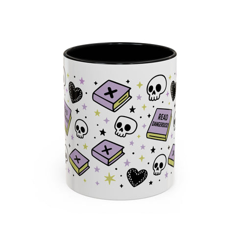 The Gothic Read Dangerously Mug Accent Coffee Mug (11, 15oz) features a glossy white finish, black interior, and playful designs of purple books, skulls, hearts, stars, and a "Read Dangerous!" book—perfect for book-loving rebels. BPA-free.