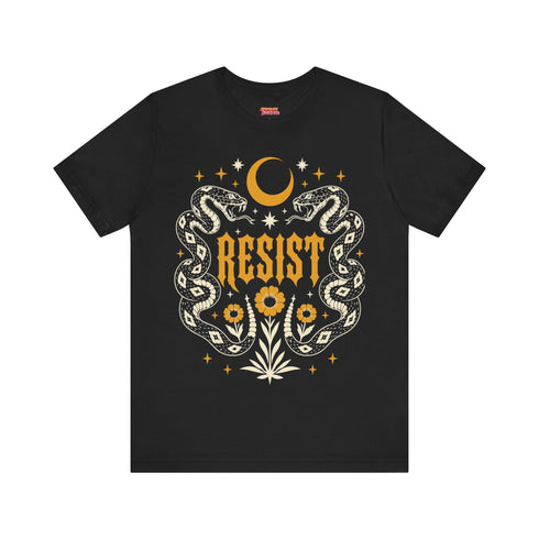 A unisex short sleeve graphic t shirt in dark charcoal black featuring a highly detailed symmetrical medallion print on the chest. In the center, the word RESIST is printed in a bold yellow gothic blackletter font. Two coiled white snakes with fine black scale details frame the text on the left and right. Above the text, a yellow crescent moon is flanked by white and yellow starbursts. Beneath, three yellow marigold flowers sit atop white stems and leafy foliage.