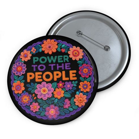 Embroidered-style pinback button featuring the phrase "POWER TO THE PEOPLE" in bold, multicolored satin-stitch letters—green, purple, and orange—framed by a vivid circular floral wreath. Pink, red, and purple flowers with leafy greens radiate around the text. Design has a handcrafted, folk-art feel with a transparent background.