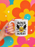 White ceramic 11oz coffee mug featuring a bold tattoo-style graphic with an angry yellow lemon face, black bat wings, and barbed wire details. The design reads “SOUR NOT SORRY” in gothic black lettering above and below the lemon. C-handle, durable construction, dishwasher and microwave safe. Graphic is high-contrast and punk-inspired, perfect for adding attitude to your drinkware collection.