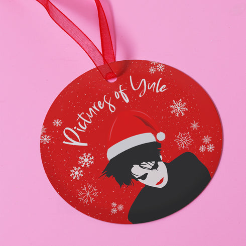 Round red metal Christmas ornament featuring Robert Smith silhouette in black with white Santa hat, red lips, and snowflake details. Text reads "Pictures of Yule" in white script.