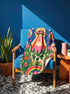 A rectangular velveteen minky blanket with a bright, maximalist design. The top half features a vibrant blue sky with a pink, green, and yellow UFO beaming rays down over hot pink snow-capped mountains. The bottom half shows a grassy green field with a white cow covered in dark spots, surrounded by large, colorful red, pink, and blue retro flowers, pine trees, and a rainbow arch at the very bottom. The reverse side is a fluffy off-white sherpa.