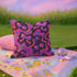 Throw pillow with a black background and a vibrant Y2K-inspired design featuring gradient cherries and shiny bows. The pattern includes pink, purple, orange, and blue psychedelic squiggles. The square pillow is displayed on a pink chair, bright blue couch, and outdoors with camping gear, emphasizing its bold, girly, and playful aesthetic. Perfect for dopamine decor, Gen Z bedrooms, or quirky home styling.