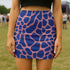 Bold high-waisted mini skirt with abstract blue giraffe spots on a pink background, perfect for festival fits and alt style lovers. Available in metallic or performance knit finishes. Sizes XS to XL.