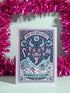 A vertical 5x7 holiday card featuring a retro tattoo style illustration of Krampus in pastel pink, teal, and black ink on shimmery silver pearlescent paper. The central horned demon has a long tongue and is surrounded by vintage rotary phones, daggers, candy canes, and skull gifts. Top text asks Have You Been Good while the bottom banner reads Krampus Is Calling. The interior text reads Let's be honest... Being good is overrated. Merry Christmas.