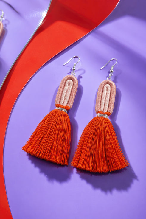 A pair of red tassel earrings with a tassel at the end, displayed on a purple background with a red and purple curved line.