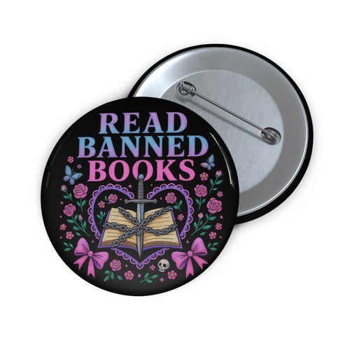 Glossy black pinback button that says “Read Banned Books” in purple and teal letters, featuring a chained book, roses, bows, and floral accents, styled on colorful books and pastel backgrounds.