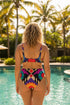 Two piece high waisted bikini in a bold 70s psychedelic geometric print. The sporty scoop top features bright yellow and red sunbursts over a black, purple, cream, and red colorblock background. The high cut bottoms carry matching geometric diamonds with hot pink and teal abstract palm leaves. Smooth form fitting recycled polyester fabric with UPF 50 sun protection and removable padding. Vibrant maximalist retro swimwear in saturated primary and secondary shades, made for pool parties, festivals, and loud s