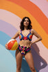Two piece high waisted bikini in a bold 70s psychedelic geometric print. The sporty scoop top features bright yellow and red sunbursts over a black, purple, cream, and red colorblock background. The high cut bottoms carry matching geometric diamonds with hot pink and teal abstract palm leaves. Smooth form fitting recycled polyester fabric with UPF 50 sun protection and removable padding. Vibrant maximalist retro swimwear in saturated primary and secondary shades, made for pool parties, festivals, and loud s