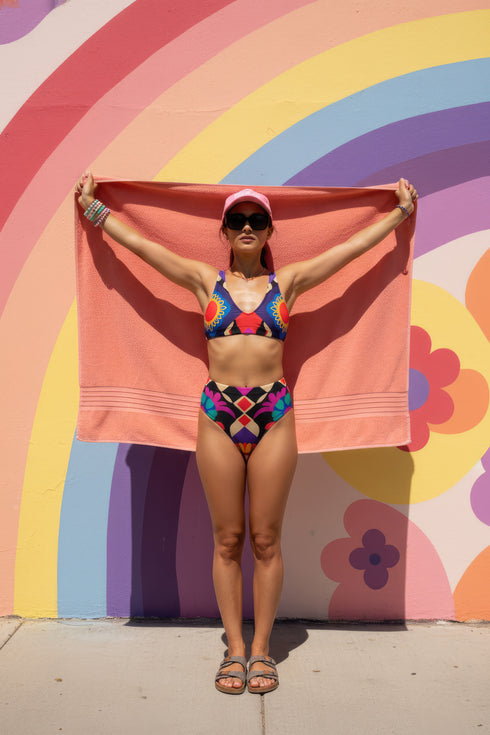 Two piece high waisted bikini in a bold 70s psychedelic geometric print. The sporty scoop top features bright yellow and red sunbursts over a black, purple, cream, and red colorblock background. The high cut bottoms carry matching geometric diamonds with hot pink and teal abstract palm leaves. Smooth form fitting recycled polyester fabric with UPF 50 sun protection and removable padding. Vibrant maximalist retro swimwear in saturated primary and secondary shades, made for pool parties, festivals, and loud s
