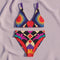 Two piece high waisted bikini in a bold 70s psychedelic geometric print. The sporty scoop top features bright yellow and red sunbursts over a black, purple, cream, and red colorblock background. The high cut bottoms carry matching geometric diamonds with hot pink and teal abstract palm leaves. Smooth form fitting recycled polyester fabric with UPF 50 sun protection and removable padding. Vibrant maximalist retro swimwear in saturated primary and secondary shades, made for pool parties, festivals, and loud s