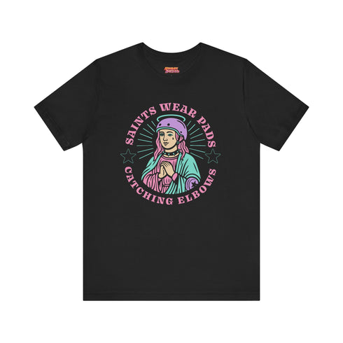 Black unisex t-shirt with bold graphic that reads "Saints Wear Pads Catching Elbows" surrounding a pastel saint figure wearing a roller skate helmet and protective pads. The design mimics embroidery in a retro tattoo-inspired art style. Available in sizes S to 3XL, this skate tee is soft, comfortable, and perfect for roller derby lovers, punk skaters, and feminist fashion fans. Great birthday or skate party gift idea.