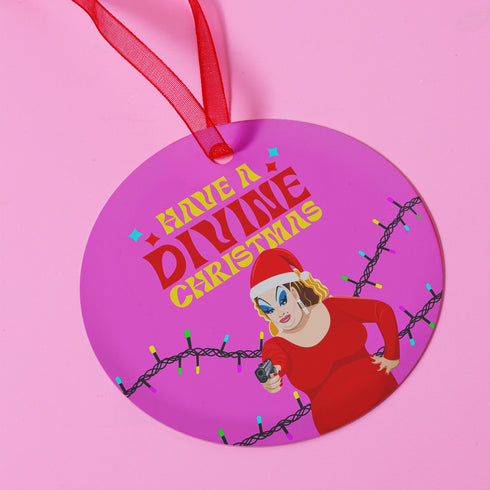 Round purple metal Christmas ornament featuring Drag Queen Divine in Santa hat and red dress with colored Christmas lights. Text reads "Have A Divine Christmas" in retro psychedelic lettering.