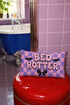 Pastel goth lumbar pillow, 20 by 12 inches, with a pink and lavender purple wavy checkerboard background. The words Bed Rotter appear in dripping pink bubble letters with a faux embroidery thread texture and black outlines. Two black bats with pink stitch details flank the text, and a black bow with a pink heart center sits below. Double sided flat print that mimics raised embroidery on linen feel polyester with a hidden zipper, insert included.