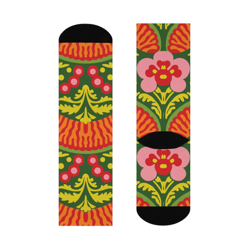 Mid-calf crew sock with a bold retro 70s maximalist botanical print. A deep green base is packed with golden yellow fern-like leaves, pink folk-style flowers with red centers, and clusters of round red and pink berries. Orange and red shell motifs with wavy stripes band the cuff and lower sock. The toe and heel are solid black. The fabric is a soft, stretchy printed knit, made as a one-size unisex statement sock for maximalist and dopamine dressing looks.
