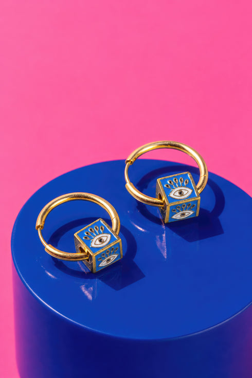 a pair of gold hoop earrings with blue eye-shaped charms on a blue circular surface.