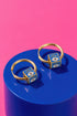 a pair of gold hoop earrings with blue eye-shaped charms on a blue circular surface.