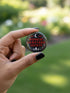A collection of four glossy black circular pinback buttons featuring striking red and white gothic illustrations. One button shows "Midnight Graveyard Society" text with bats and tombstones. Another reads "Cemetery Picnic Society" with a coffin and umbrella icon. A third features a detailed white skull and red roses with "Memento Mori" text below. The final pin displays "Nocturnal Flower Society" surrounded by floral vines.