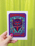 A vertical 5x7 inch folded greeting card featuring a detailed, psychedelic illustration of the folklore figure Krampus for a New Year celebration. The card stock has a shimmering pearlescent finish that reflects light, creating a glowing effect on the purple and teal artwork. The design mimics a vintage event poster reading "Krampus Ball 2026" and "Entry Fee: One Naughty Soul" in retro fonts. Krampus is depicted with large horns, sunglasses, and a long tongue holding a candy cane.