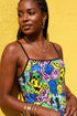 A sleeveless women's camisole top featuring a pointed handkerchief hemline often called a bandana top style. The fabric displays a vibrant all-over psychedelic print of distorting and melting smiley faces mixed with melting skulls. The color palette includes bright neon yellow, electric blue, hot pink, and lime green against a multi-colored background. The top features thin black adjustable spaghetti straps and black trim along the straight neckline. The fit is cropped and form-fitting.