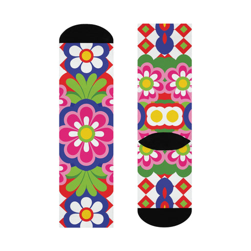Mid-calf crew sock with a bold 70s psychedelic floral print. The design mixes a red and white diagonal checkerboard with oversized retro flowers, including white daisies with bright yellow centers and a large hot pink bloom with a white inner layer, set over a royal blue background with green leafy foliage. The toe and heel are solid black. The fabric is a soft, stretchy printed knit, made as a one-size unisex statement sock for maximalist and dopamine dressing looks.
