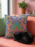 A square decorative throw pillow cover featuring a highly symmetrical bright octopus design. The octopus has a turquoise blue body with a diamond patterned head and eight curled tentacles detailed in bright pink and lime green. The background is a repeating diamond argyle pattern in royal blue and light pink. The artwork is a flat two dimensional print that mimics the textured look of intricate crewelwork embroidery. The pillow features a hidden zipper on the bottom edge. No insert included.