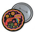 Round pinback button badge with a black background, featuring a retro illustration of a red revolver shooting out a rainbow flag that says “LOVE.” Surrounded by colorful 70s-style flowers and peace signs, outlined in wavy neon border. Glossy finish with vibrant pop colors and psychedelic design.