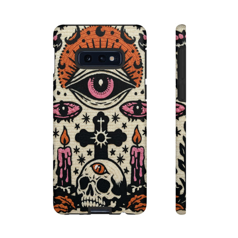A vertical phone case design featuring a faux crochet texture illusion printed on a cream background. The symmetrical pattern centers on a large black eye with a pink iris and rust-orange sunburst lashes at the top. Below the eye is a black cross surrounded by small black stars. The bottom features a skull with a third rust-orange eye on its forehead. Flanking the skull are two candles with orange flames and rust-colored leaves. The design mimics the look of stitched yarn but is a 2d print.