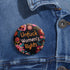 Round pinback button with black background featuring vibrant floral embroidery design surrounding bold orange and white text reading "Unfuck Women's Rights" - feminist protest accessory with glossy finish, safety pin backing, available in 2" and 3" sizes for jackets, bags, and activist wear.
