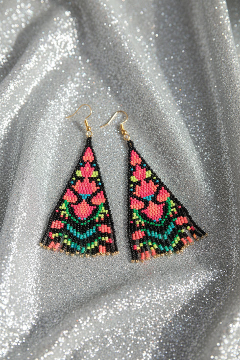 A pair of colorful, beaded earrings with a floral pattern rests on a glittery surface.