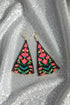 A pair of colorful, beaded earrings with a floral pattern rests on a glittery surface.