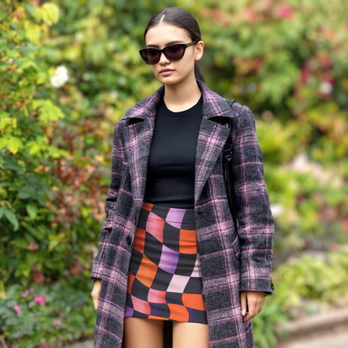 Honey Dazed mini pencil skirt featuring a bold wavy checkerboard pattern in black, orange, purple, and pink. Made from soft eco-polyester with a curve-hugging stretch fit and a flattering high-waist silhouette. The print has a slightly glossy finish, giving it a sleek and modern look. Designed for festival fits, streetwear moments, and retro rave energy. A vivid, sculptural mini skirt that pairs easily with crop tops and confident energy.