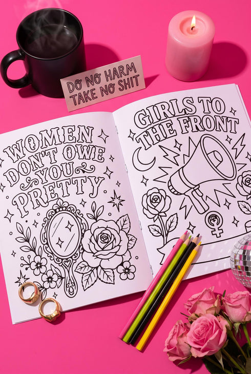 A 8.5 by 11 inch softcover coloring book titled The Feminist Rage Coloring Book For Cute Loud Unhinged Women. The black cover features vibrant pink and green typography, a fanged heart engulfed in flames, pink roses, and crescent moons. The back cover displays a heart pierced by a dagger and text reading Your feelings are valid your rage is too. Inside pages contain black and white line art with bold feminist quotes, floral borders, potions, coffins, and edgy witchy illustrations.