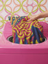 A square decorative throw pillow cover featuring a trippy retro Bigfoot scene. A large navy blue silhouette of Sasquatch walks through a forest of navy and yellow pine trees. The background is a psychedelic swirling sky in vibrant pink and yellow, featuring a large stylized eye and a cluster of small yellow stars. The flat two dimensional print visually mimics the textured look of heavy needlepoint embroidery. The pillow features a sleek hidden zipper on the bottom. No insert is included.