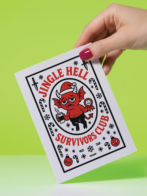 A 5x7 pearlescent shimmer folded greeting card featuring the Jingle Hell Survivors Club design. The front is a illustration of a grumpy red devil imp character, wearing a small Santa hat, holding a coffee cup, and a circular 'I Tried' merit badge. The overall aesthetic is maximalist dark humor and spooky cute. This anti-Christmas card is perfect for those needing relief from holiday stress. Inside text references surviving tolerable relatives, strong eggnog, and merciful hangovers.