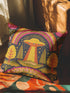 A colorful throw pillow with a vibrant alien design and a rainbow-colored background, resting on a patterned fabric.