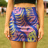 High-waisted mini skirt with a vibrant pastel tiger stripe pattern in electric blue, soft pink, yellow, and violet. The bodycon silhouette hugs curves with a comfy elastic waistband and stretch fabric. Available in smooth performance fabric or glitter finish. A maximalist fashion piece for festivals, summer outfits, and ravewear.