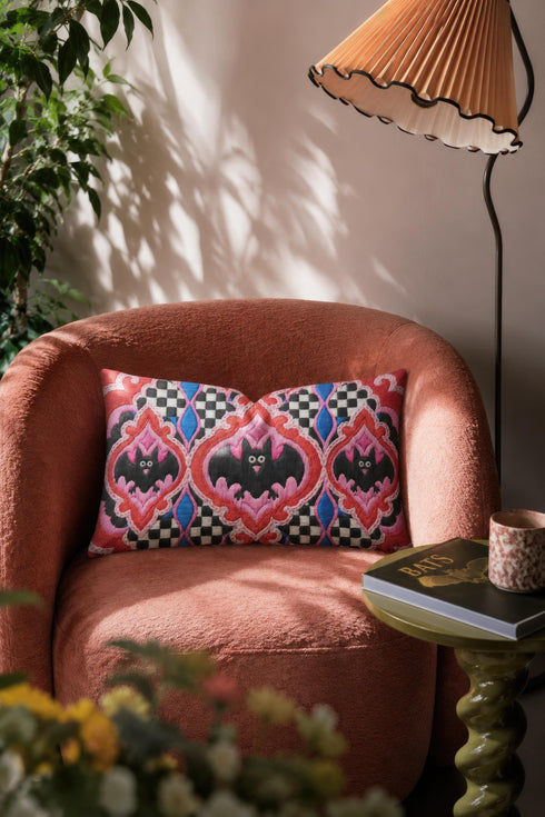 Rectangular 20x12 inch lumbar pillow cover in red featuring printed faux embroidery of three black bats with white eyes and pink noses, each framed in an ornate ogee medallion with pink flame stitch centers, black and white checkerboard accents, and cobalt blue diamonds. Whimsigoth damask bat design printed on both sides with a hidden zipper, crafted from soft linen look polyester for spooky maximalist home decor.