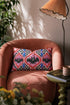 Rectangular 20x12 inch lumbar pillow cover in red featuring printed faux embroidery of three black bats with white eyes and pink noses, each framed in an ornate ogee medallion with pink flame stitch centers, black and white checkerboard accents, and cobalt blue diamonds. Whimsigoth damask bat design printed on both sides with a hidden zipper, crafted from soft linen look polyester for spooky maximalist home decor.