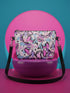 Small vegan leather crossbody purse with a real pebble grain texture and adjustable black strap. The flat printed artwork features a scattered all over pattern of pink skulls, purple and pastel blue winged bats, pink fanged mouths, and loose eyeballs set against a cream colored background. The bag is shown with black and silver hardware including a black top zipper, black zipper pull, black strap tabs, and silver metal rings and clips. The compact rectangular bag measures 8.5 by 7 by 2 inches.