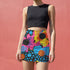 A woman wearing a black crop top and a colorful, patterned mini skirt stands against a pink wall.