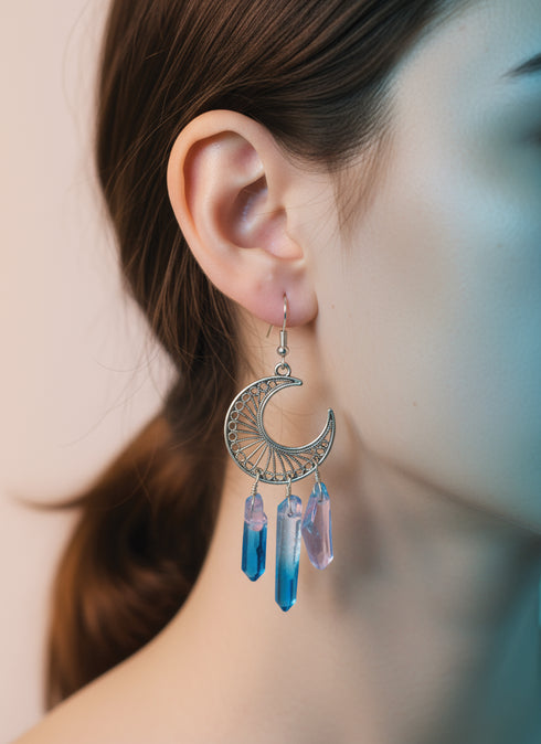 A close-up of a woman's ear wearing a pair of silver earrings with blue and purple crystals hanging from them.