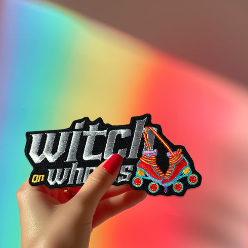 Embroidered patch featuring 'Witch on Wheels' text in metallic silver and white. Colorful roller skate design with vibrant rainbow hues. Fun, retro-inspired accessory for skaters and witchy enthusiasts. Ideal for jackets or bags.