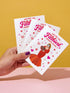 A 5x7 inch pearlescent silver greeting card featuring a flat vector illustration of the drag queen Divine in a red mermaid gown holding a heart-shaped box of chocolates. The text above reads "You're The Filthiest Person Alive" in bold red script with pink sparkles. The card has a shimmering finish that reflects light. Inside text reads "...and I love it." The back features the Honey Dazed logo. Includes a matching envelope.