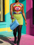 A sleeveless scoop neck crop top featuring a bold all-over printed design. The central graphic is a large bright red heart enclosing a scalloped pink flower shape and a blue evil eye motif in the middle. The background surrounds the heart with mirrored concentric wavy arches and scalloped borders in vibrant shades of lime green, pink, blue, and red. The fitted garment has a smooth athletic texture. Available in a standard matte performance knit or a sparkly silver glitter foil finish.