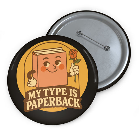 A glossy black round pin-back button with a retro 1970s-style design. The center shows a smiling cartoon paperback book holding a red rose, colored light brown with white gloves and feet. Below, “MY TYPE IS PAPERBACK” appears in chunky brown-and-tan 70s lettering. This bookish flair piece has a high-gloss, scratch-resistant mylar finish, secure safety pin backing, and comes in two- or three-inch sizes.